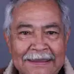 Close-up of an elderly man with a warm smile, gray hair, and a mustache, representing quality dental care.